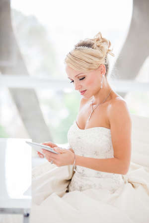 Gorgeous smiling blonde bride  with a Mini touch pad in a Penthouse  at a modern hotel messaging her Husband I Love You!の写真素材
