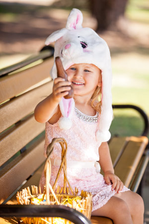 Cute  young girl in a Bunny hat smiling in the park holding a chocolate Easter Bunny