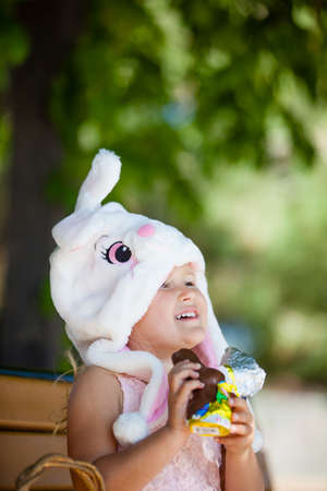 Cute  young girl in a Bunny hat smiling in the park unwrapping a chocolate Easter Bunnyの写真素材