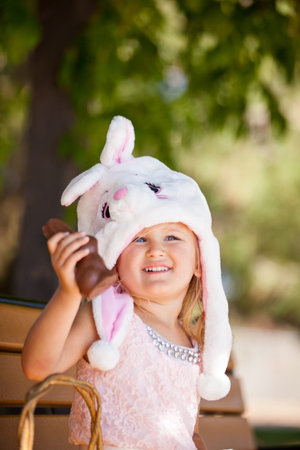 Cute  young girl in a Bunny hat smiling in the park holding a chocolate Easter Bunny
