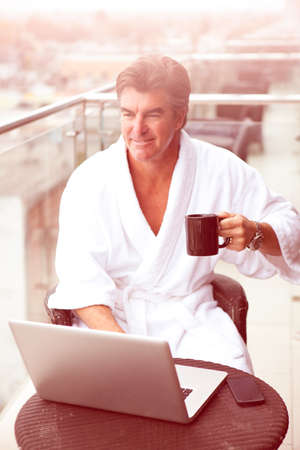 Attractive Man enjoying his morning coffee on his computer outside his hotel roomの写真素材