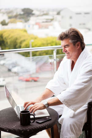 Attractive Man enjoying his morning coffee on his computer outside his hotel roomの写真素材