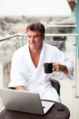 Attractive Man enjoying his morning coffee on his computer outside his hotel roomの写真素材