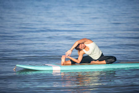 Pretty woman in side bend doing SUP Yoga on the waterの写真素材