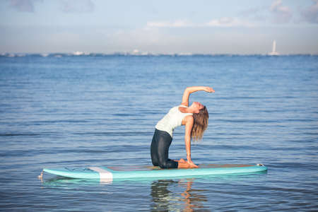 Pretty woman in back bend doing SUP Yoga on the waterの写真素材