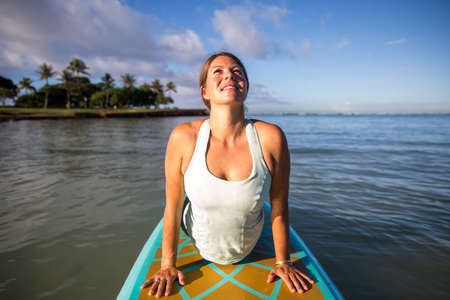 Pretty woman in cobra position doing SUP Yoga on the waterの写真素材