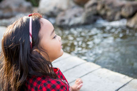 Cute little girl looking into the pond and makes a wishの写真素材