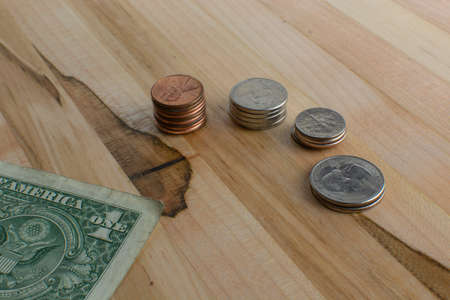 US pocket change arranged in small stacks along with a folded dollar bill placed on a wooden table.の写真素材