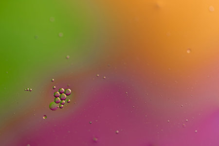 A closeup of oil droplets on a water surface with a colored background.