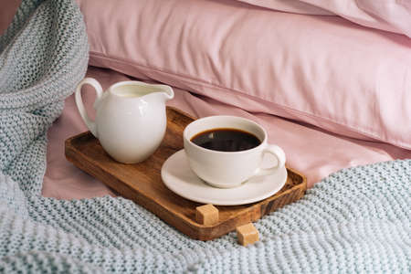 Breakfast in bed with freshly brewed and delicious coffee, a jug of cold milk and cane sugar on a wooden tray against a backdrop of pink sheets, pillows and a blue plaid. Horizontalの写真素材