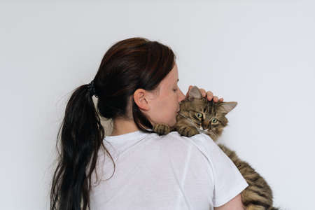 A young brunette girl in a white T-shirt holds on the shoulder of a sad green-eyed cat and strokes himの写真素材