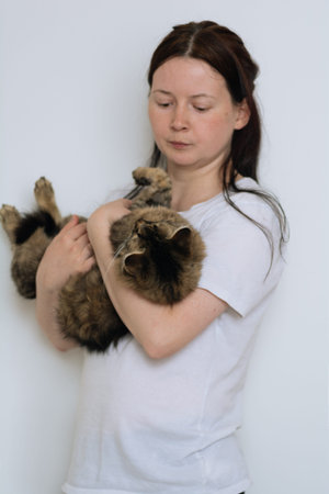 young girl with dark hair and white T-shirt holds a fluffy and cute cat