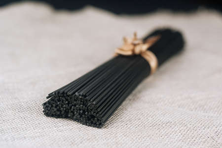 Raw black homemade spaghetti bunch on canvas rag. Dry black noodles macaroni bundle.の写真素材