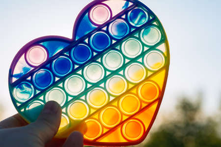 colorful antistress sensory toy fidget push pop in hand on sky background. rainbow pop heartの写真素材
