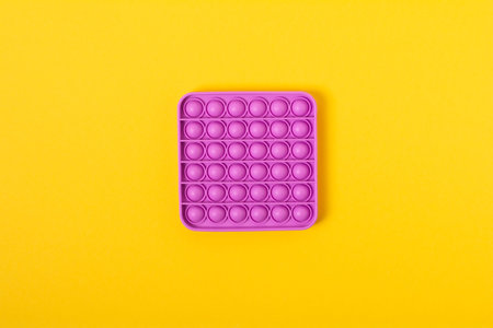 Top view Pop it fidget toy on a empty copy space yellow background. Multicolored antistress toy flat...
