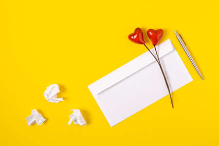 top view love letter draft, white envelope with red hearts on yellow background. white letter with copy space flat layの写真素材