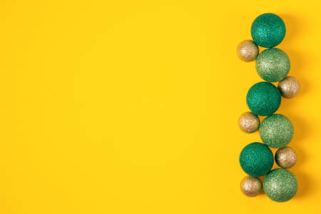 Christmas and Happy new year green and gold balls flat lay on yellow background. Xmas card decoration with copy space.の写真素材
