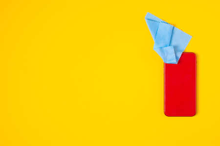 Top view cleaning smart phone screen on yellow background. Flat lay cleaning red phone by fabric microfiber conceptの写真素材