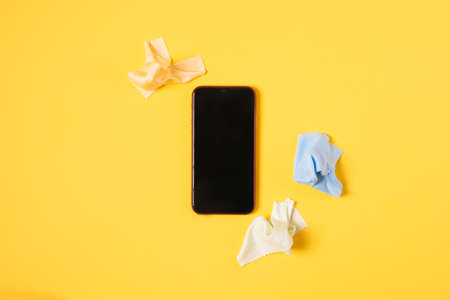 Top view cleaning smart phone screen on yellow background. Flat lay cleaning touch screen by fabric microfiber conceptの写真素材