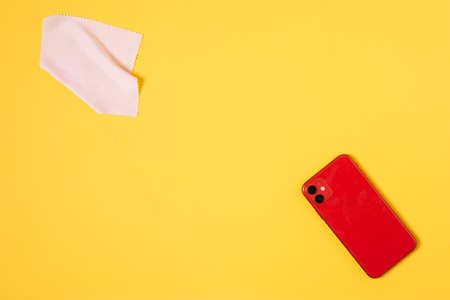 Top view cleaning smart phone screen on yellow background. Flat lay cleaning red phone by fabric microfiber conceptの写真素材