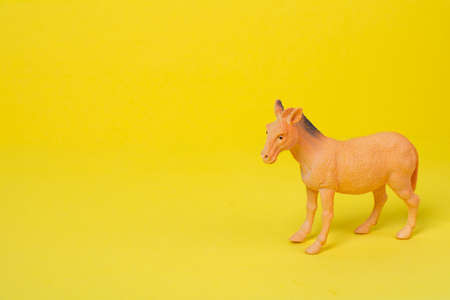 Baby toy horse made of plastic on a yellow background with copy space. Cute children toy brown horse on colored background. Baby toys conceptの写真素材