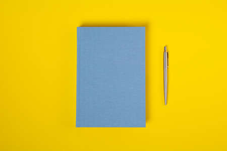 Top view closed blue notebook and pen over yellow background with copy space. Minimalist flat lay image of closed diary and pen.の写真素材