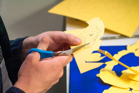 Young man makes paper figures. Boy's hands cut yellow origami with scissors. Make 3D paper figures....