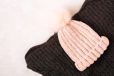 A warm hat and scarf. Winter knitted clothes on a fur white background. Knitted beautiful beige woolen hat with fur pompon ball, close-knitの写真素材