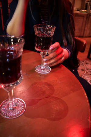 young female hands holding glass of red wine beverage liquor in dark interior restaurant, late night...