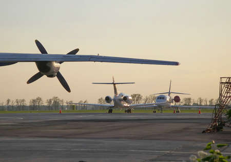 Airplane wing with propeller and two private jet aircraft on the field before sunset.の写真素材