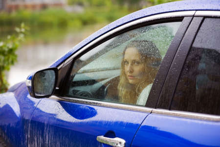 Sad young woman looking through the window with a rain drops.の写真素材