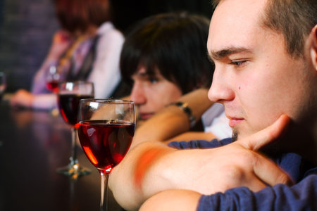 Young men drinking red wine on a bar counter.