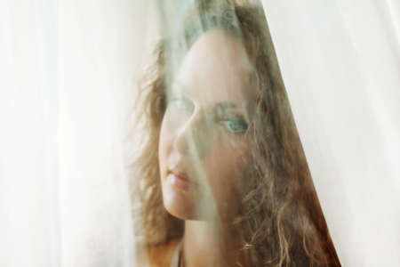 Sad beautiful woman looking through a window.の写真素材
