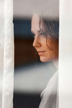 Sad woman looking through the windowの写真素材