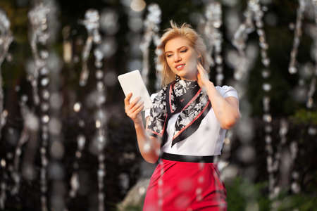 Young woman with a digital tablet computer against a city fountainの写真素材