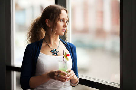 Sad woman with coctail looking out the windowの写真素材
