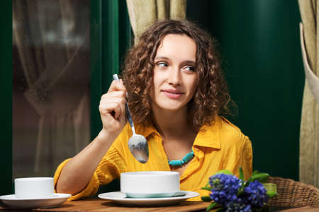 Happy young woman eating a soup at restaurantの写真素材