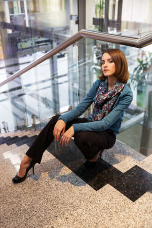 Young business woman sitting on the steps in office interiorの写真素材