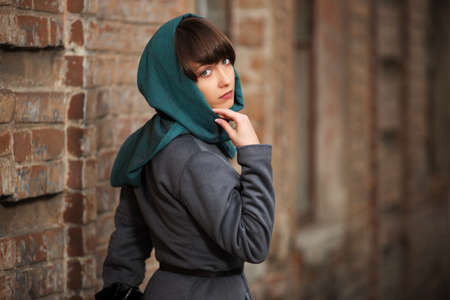 Sad young woman in grey classic coat at the wallの写真素材