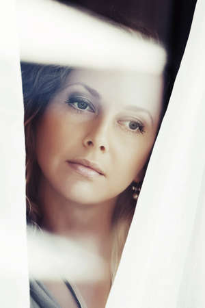 Beautiful young woman looking through the windowの写真素材