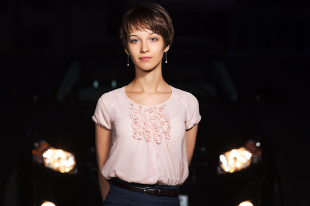Young woman in the night in front of car headlightsの写真素材