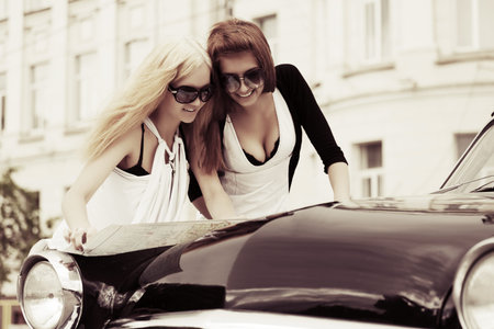 Two young women with a road map at the retro car