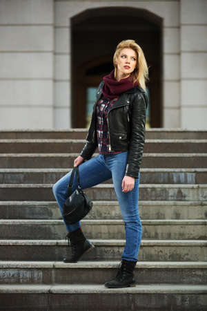 Young fashion blond woman in leather jacket on the stepsの写真素材