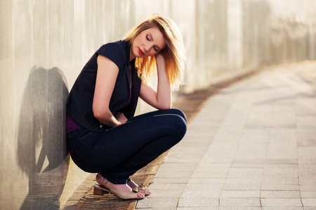 Sad young fashion blond woman sitting at the wallの写真素材