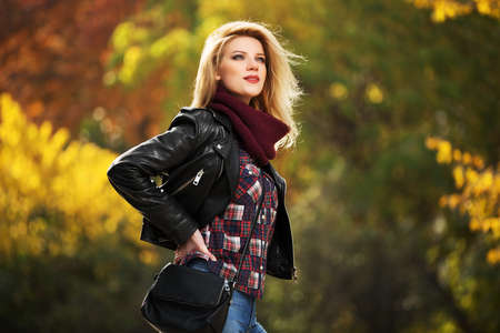 Young fashion blond woman in leather jacket in autumn parkの写真素材