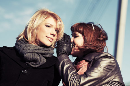 Two happy young fashion women teeling secrets outdoorの写真素材