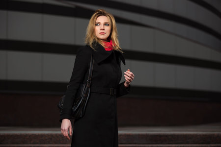 Fashion blond woman in black coat walking on night city street