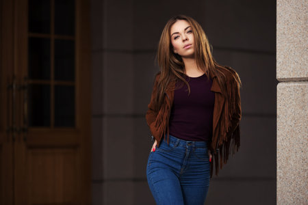Young fashion woman in red leather jacket walking on city street