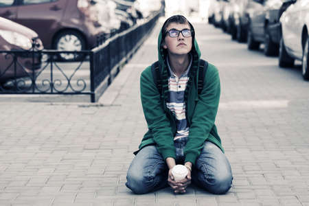 Portrait of young fashion man sitting on a city sidewalkの写真素材