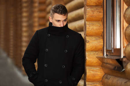 Young handsome man in classic black coat standing at the wooden wallの写真素材